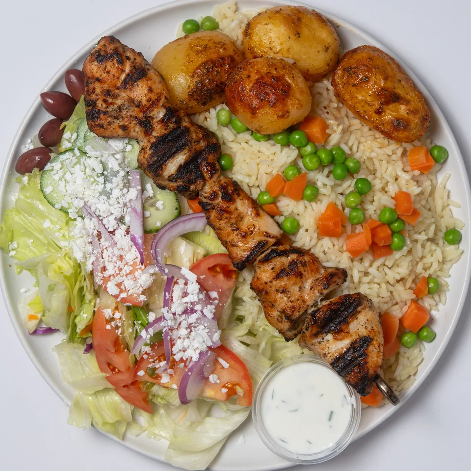 Chicken souvlaki plate: a grilled skewer over seasoned rice with peas and carrots, roasted potatoes, Greek salad and a cup of tzatziki