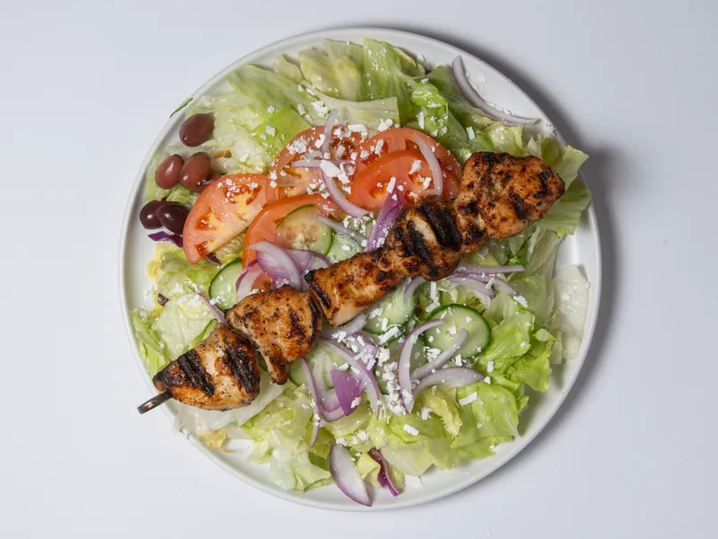 Greek salad topped with a grilled chicken souvlaki skewer
