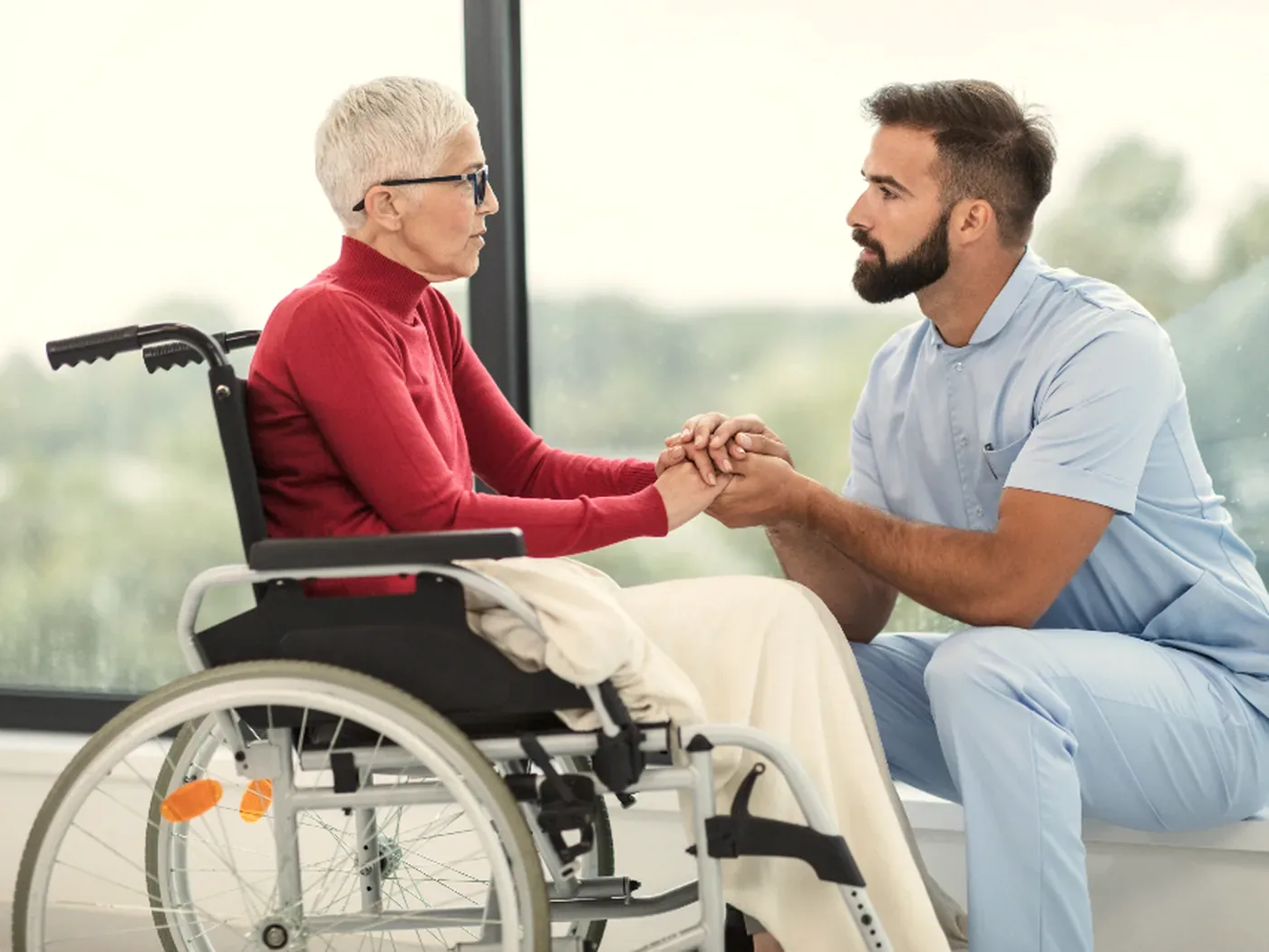 A nurse kneeling to speak with a patient in a wheelchair