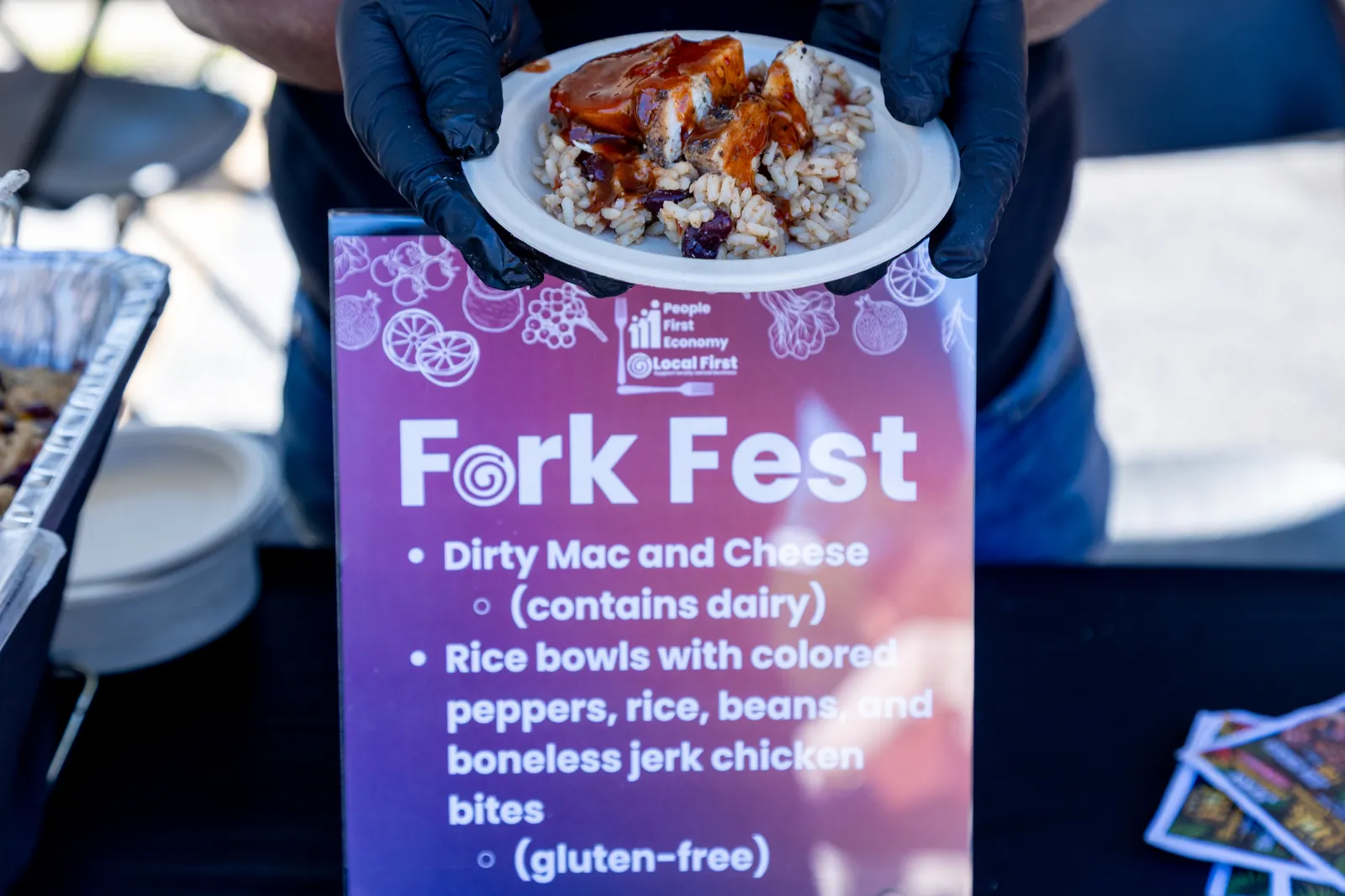A rice bowl with boneless jerk chicken bites held above the HoneyBee's Fork Fest menu sign
