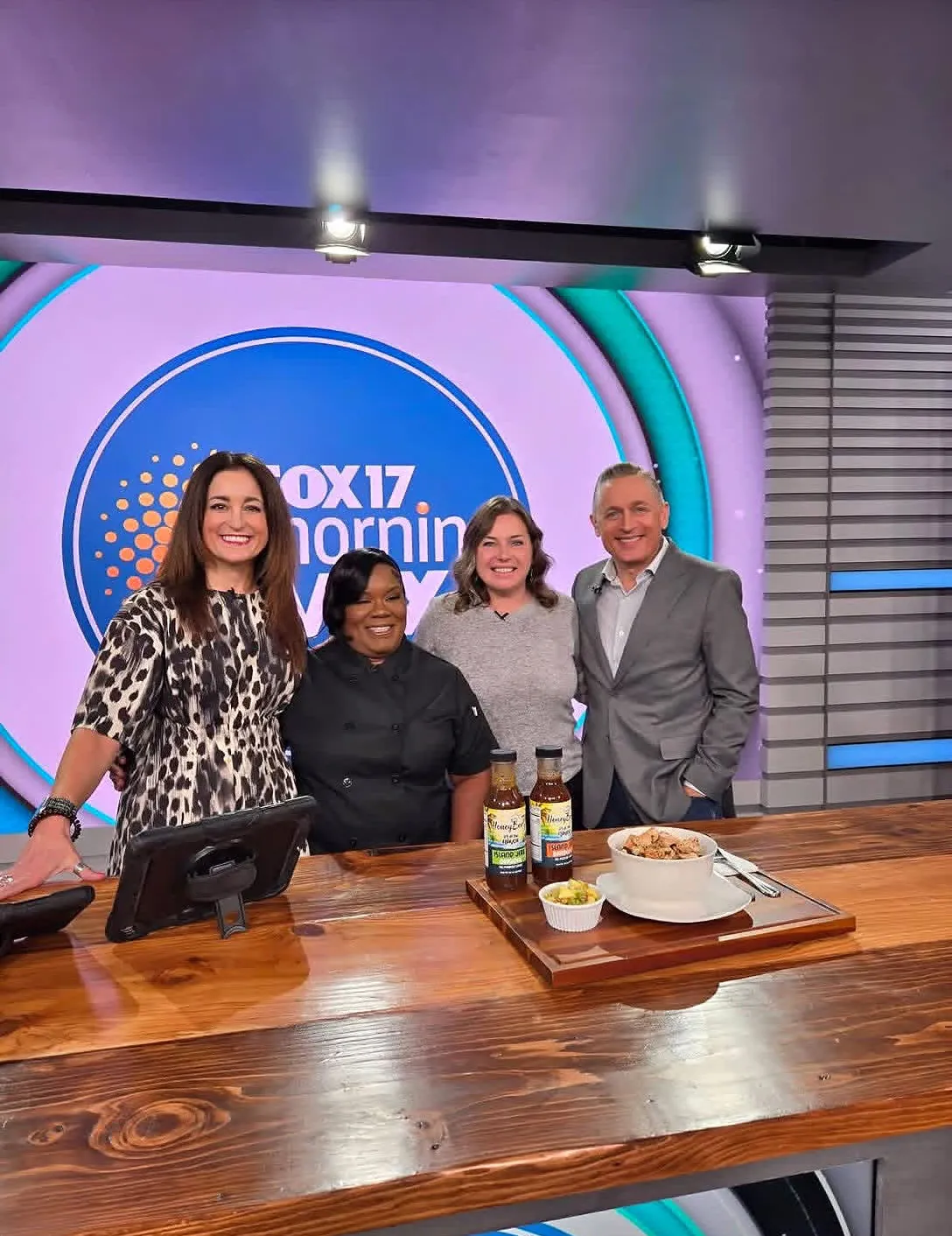 Chef Barbara Johnson on the FOX 17 Morning Mix set with the hosts and two bottles of HoneyBee's Island Sauce