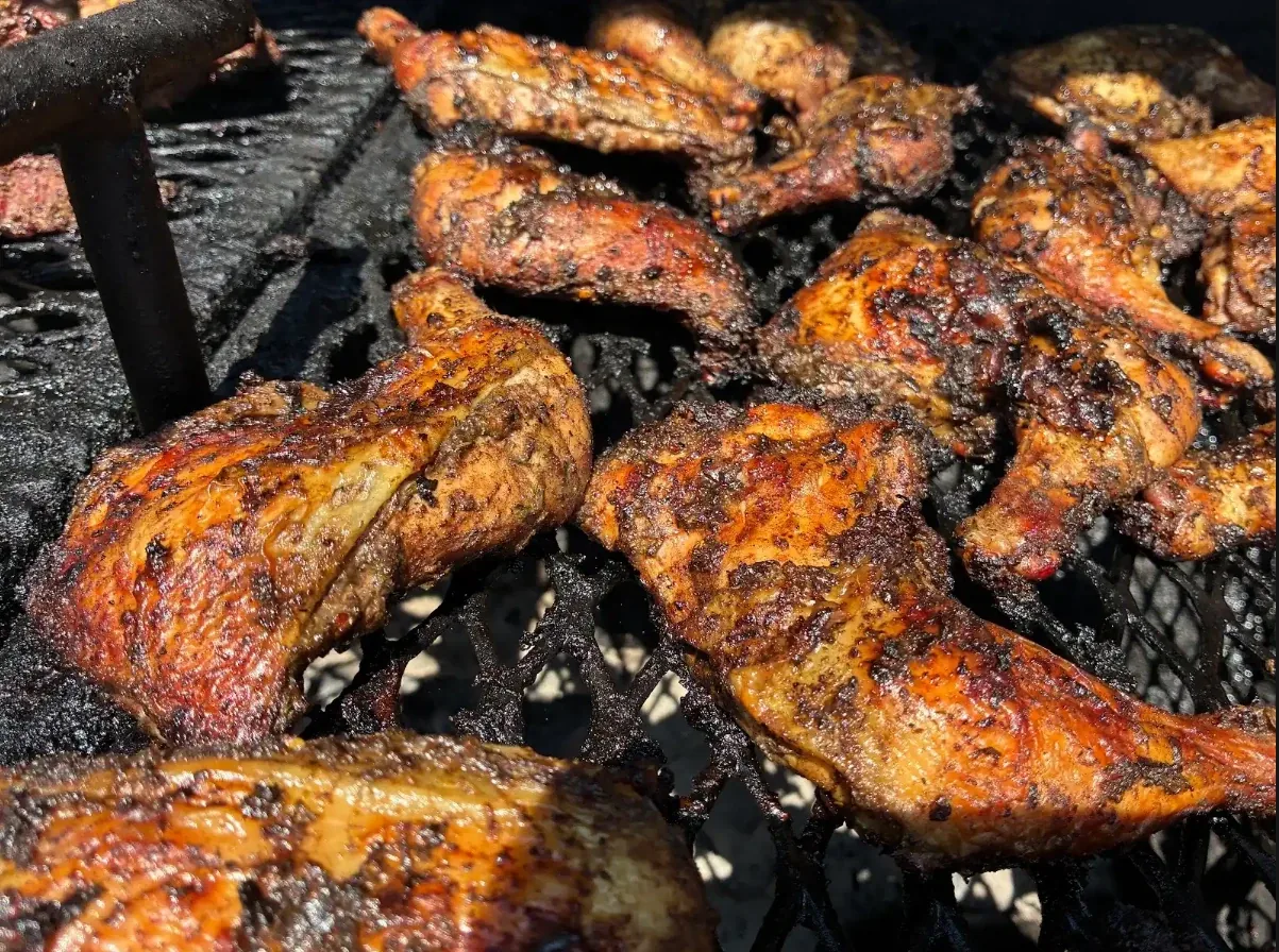 Close-up of jerk chicken quarters and wings finishing over the charcoal grill