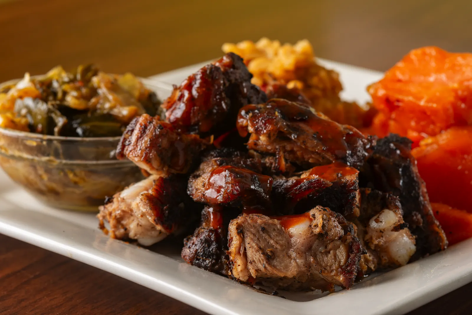 Jerk rib tips glazed with island sauce, plated with collard greens, rice and candied yams