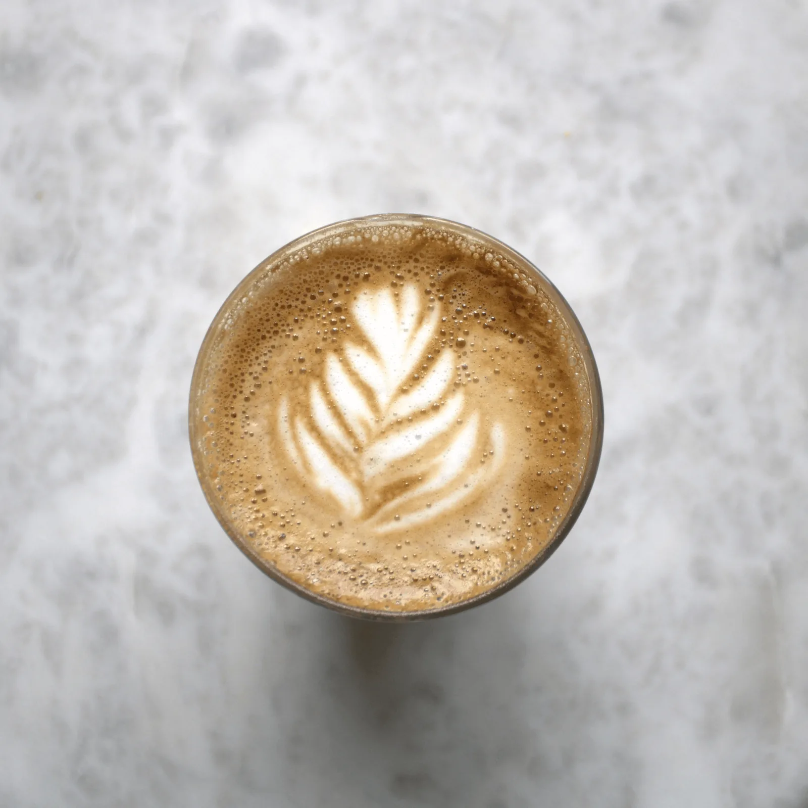 Overhead view of a latte with a delicate leaf design in the foam, on a marble surface.
