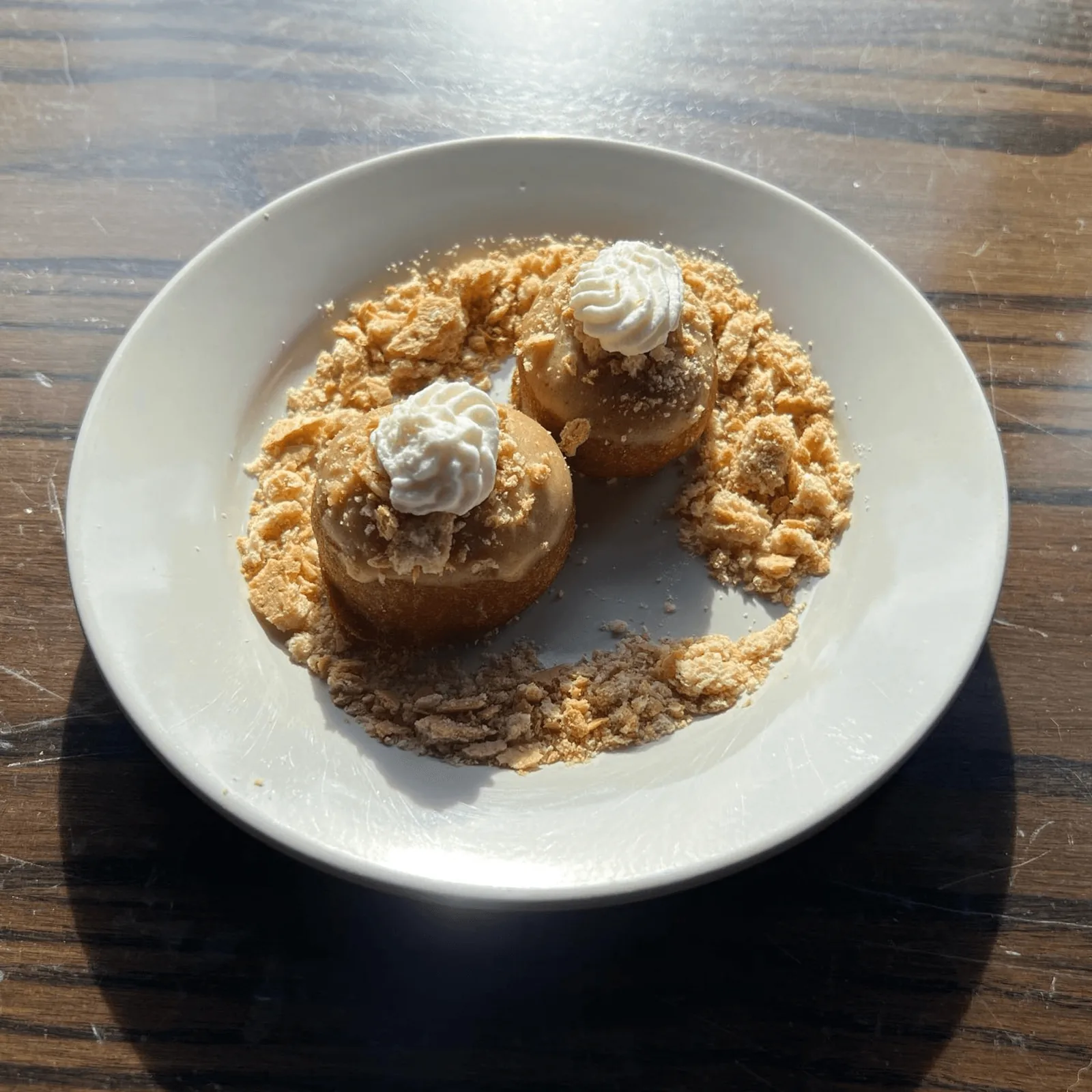 Two small, round pastries with white frosting and crumbled topping on a white plate.