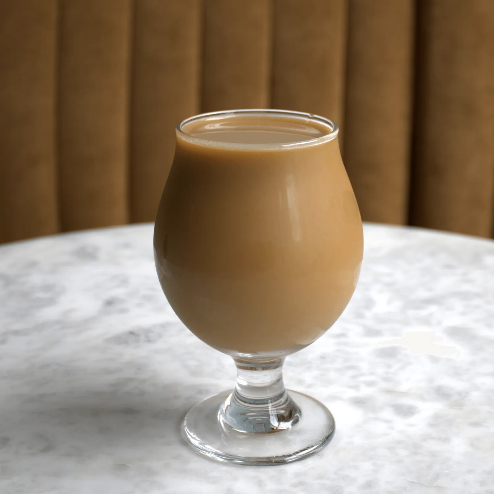 A glass of creamy Ipsento 606 coffee sits on a white marble table with a brown background.