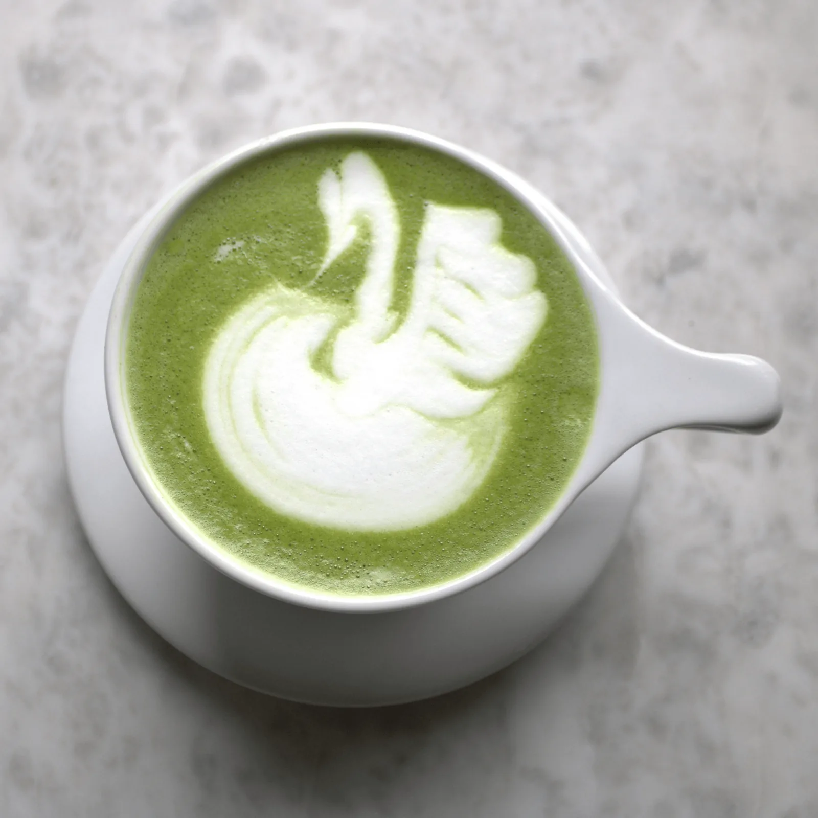 A vibrant green matcha latte with a delicate swan latte art design in a white cup.