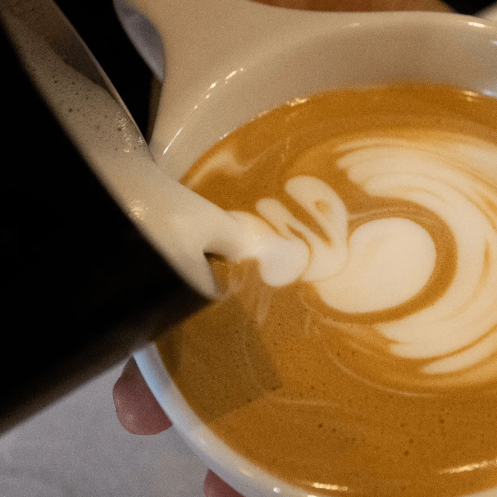 A barista pours steamed milk into a latte, creating a delicate heart-shaped latte art design.