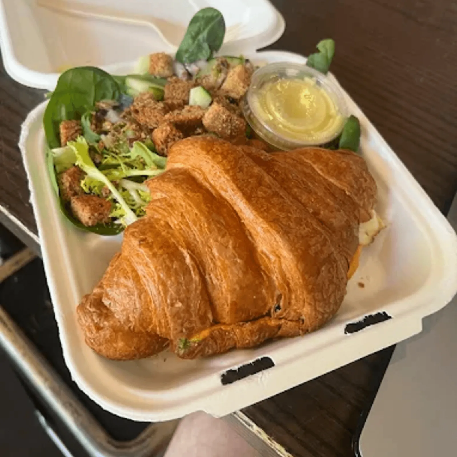 Croissant sandwich with a side salad and dressing in a takeout container from Ipsento 606.