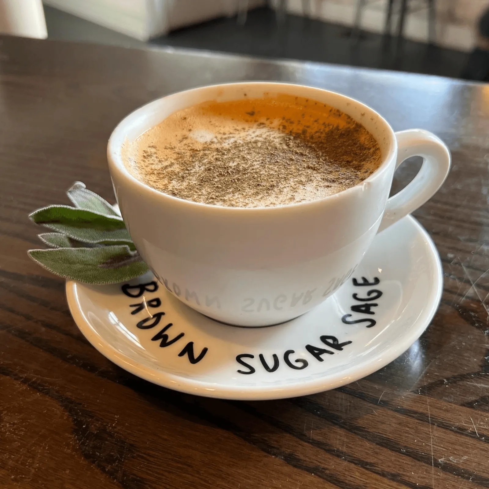 A coffee drink with foam and spice on top, served on a saucer with "BROWN SUGAR SAGE" text.