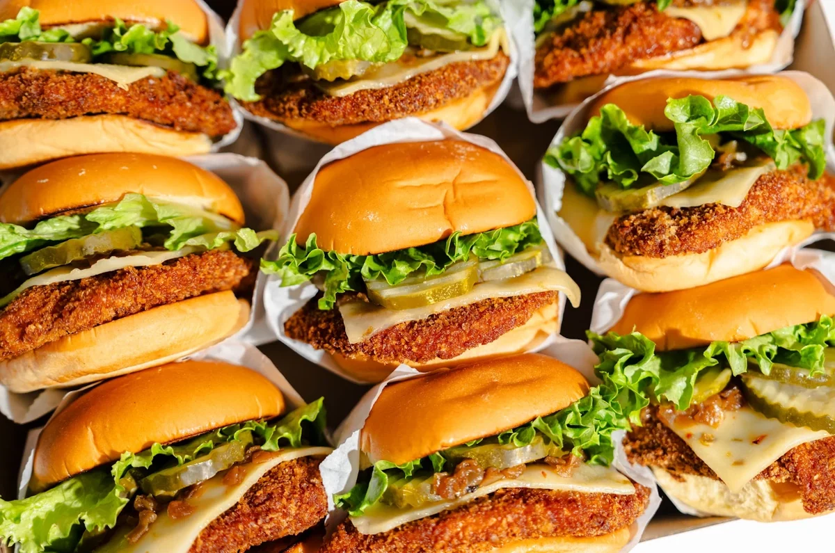 A close-up tray of crispy chicken sandwiches with lettuce, pickles and melted cheese on toasted potato buns.