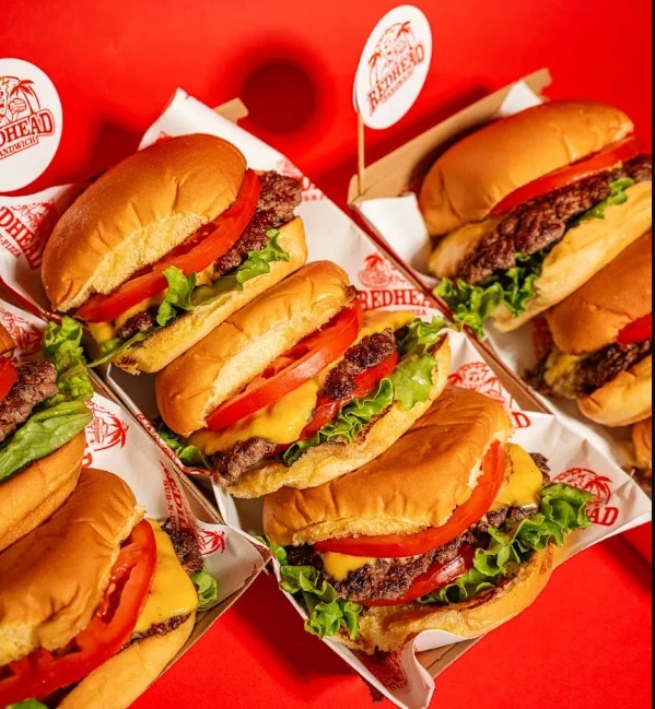Smash burgers with cheese, lettuce and tomato in Redhead Burger boats on a bright red background.