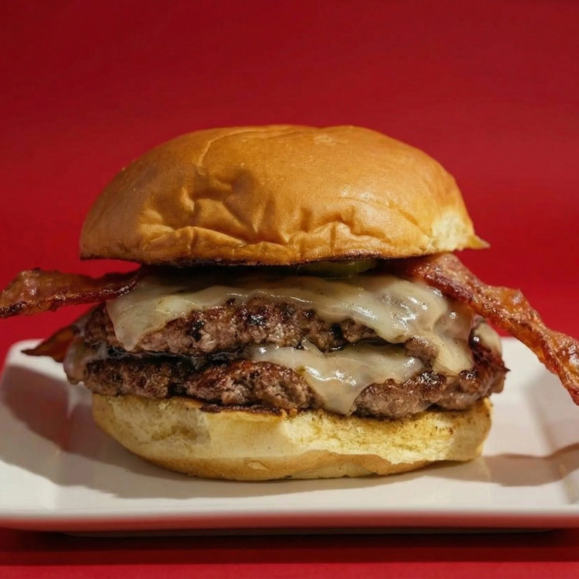Double patty RedHead Burger with melted cheese and bacon on a white plate against a red background.