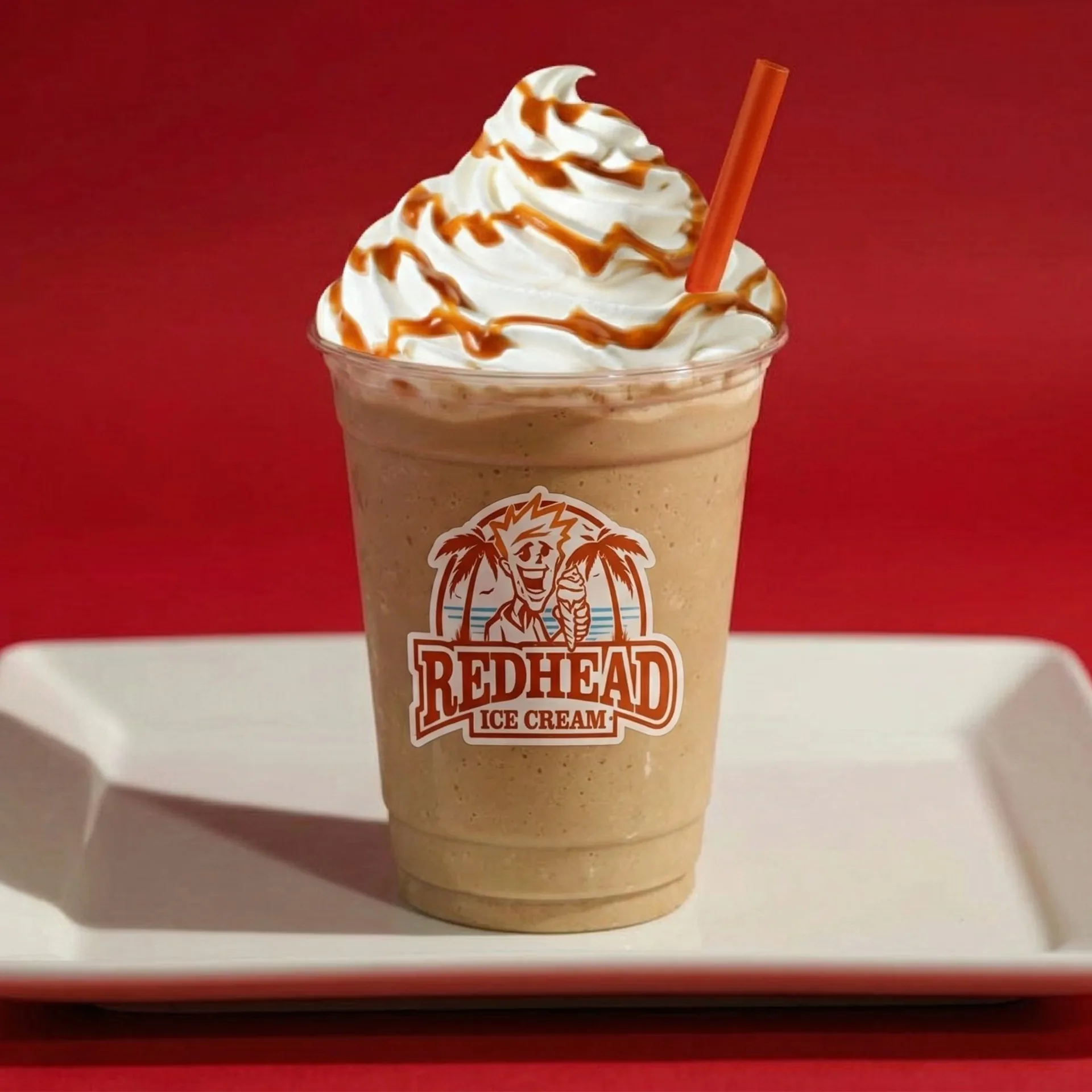 A Redhead Ice Cream milkshake with whipped cream, caramel drizzle, and an orange straw.