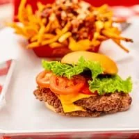 A RedHead Burger with lettuce, tomato, and cheese, next to a basket of loaded fries.