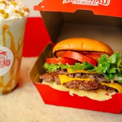A RedHead Burger with two patties, cheese, lettuce, and tomato, next to a milkshake.