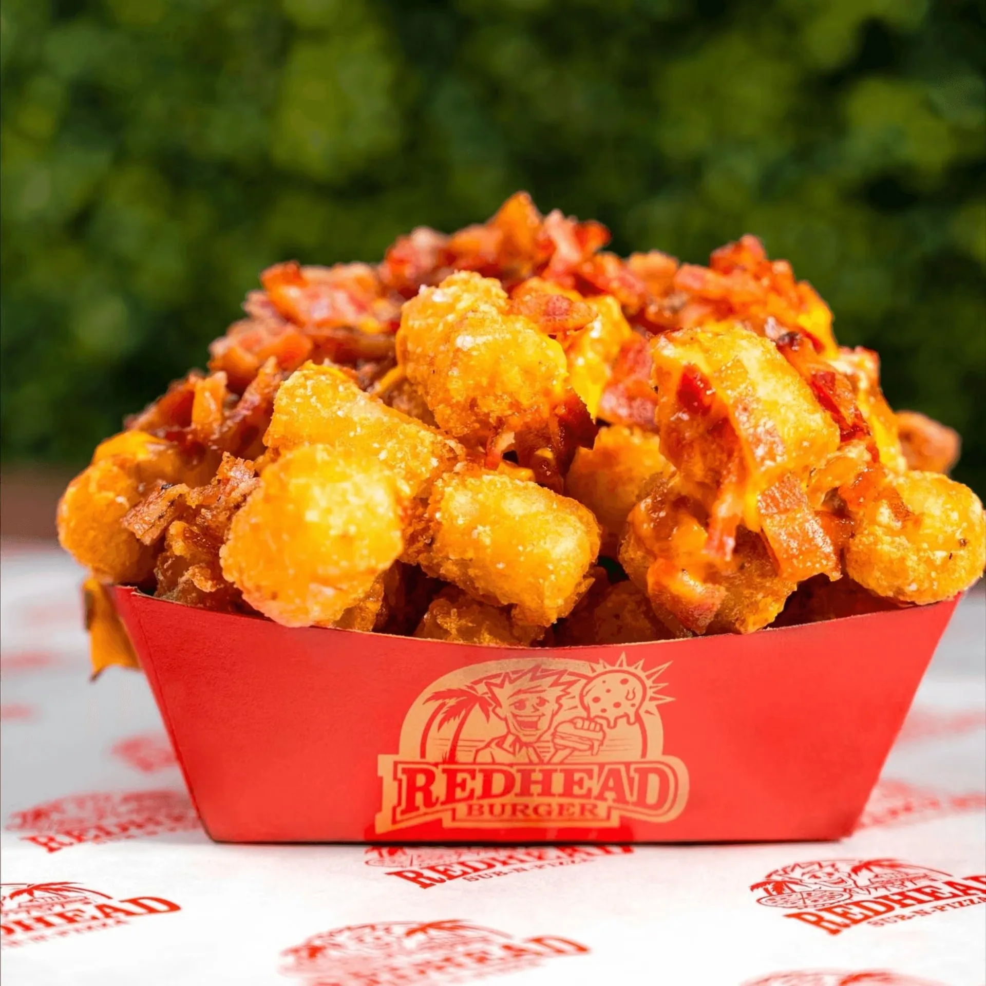 RedHead Burger's loaded tater tots with melted cheese and bacon bits in a red container.