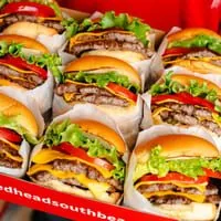 A box filled with many double cheeseburgers, each with lettuce, tomato, and cheese.