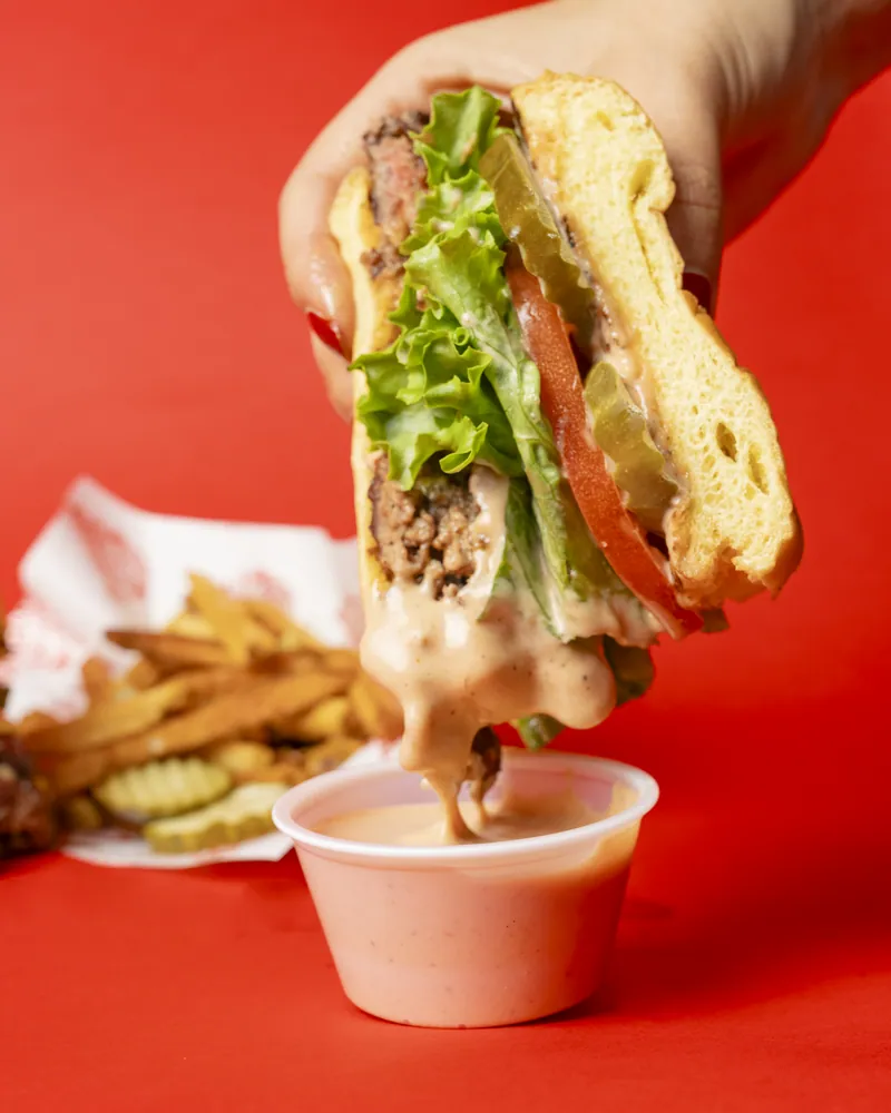 A Redhead Burger dipped into Redhead sauce with fresh-cut fries alongside