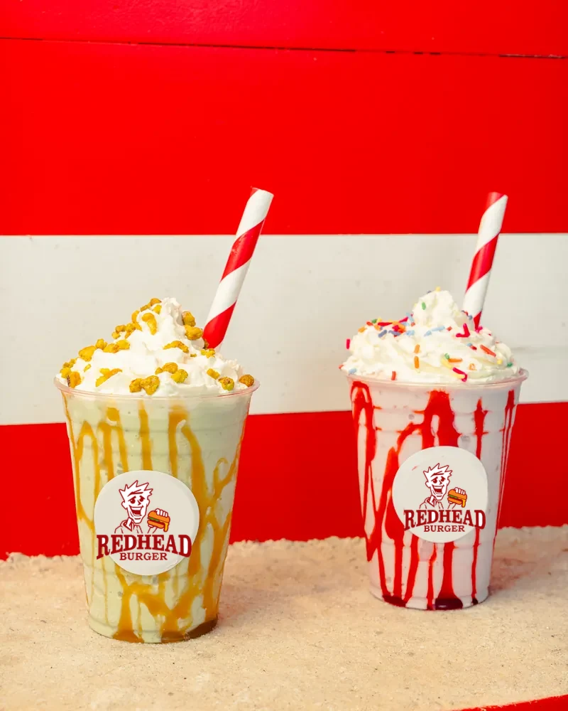 Two Redhead Burger milkshakes in striped cups against a red and white wall