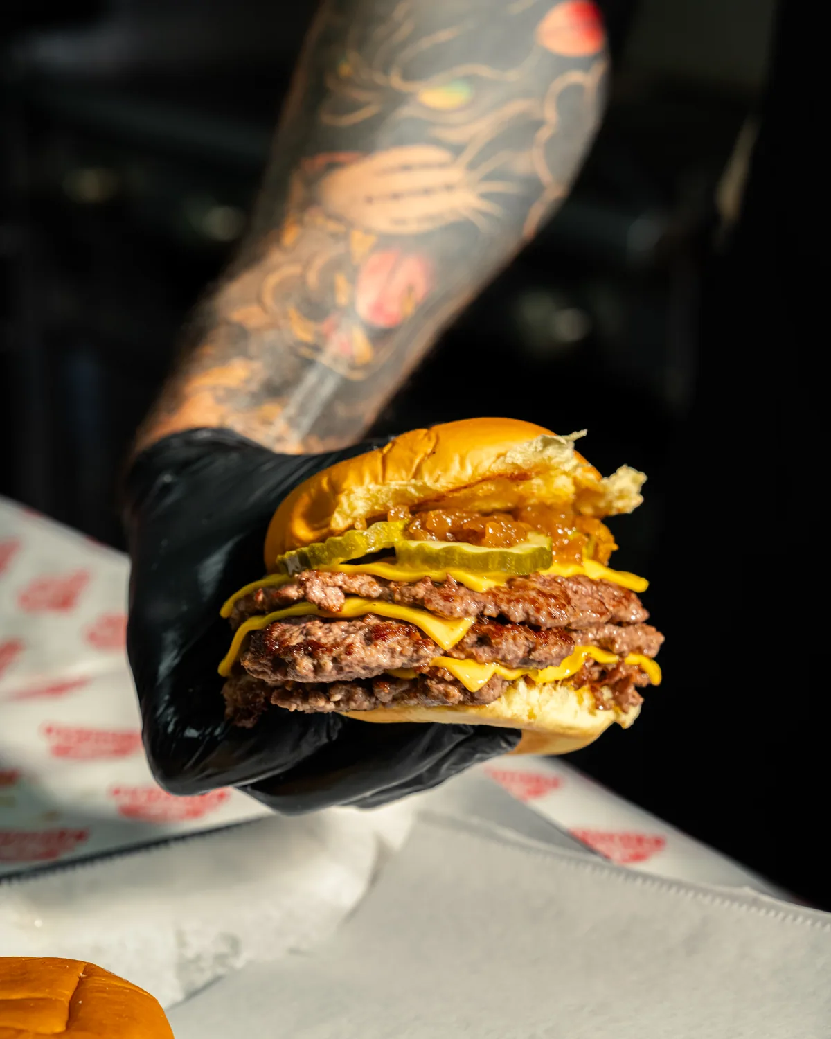 A gloved hand lifting a stacked Redhead Burger off the pass