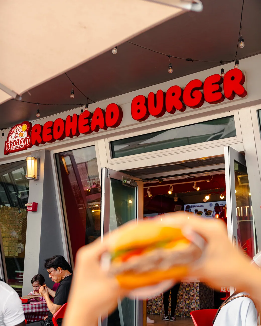 The Redhead Burger storefront on Ocean Drive, a burger held up at the window
