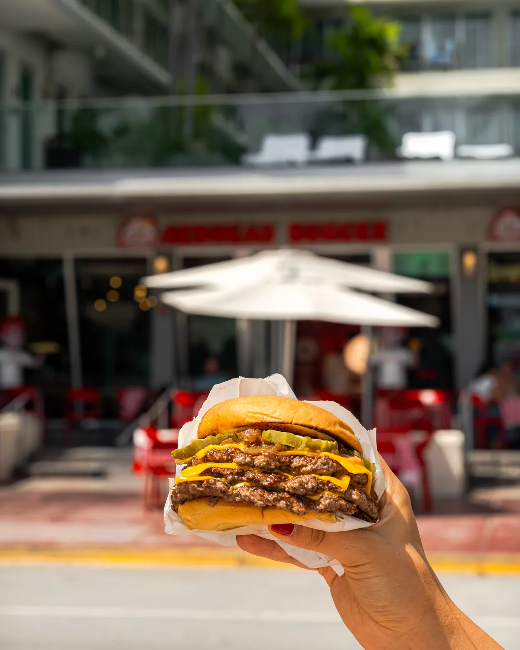 A hand holding a triple-stacked Redhead Burger outside the restaurant