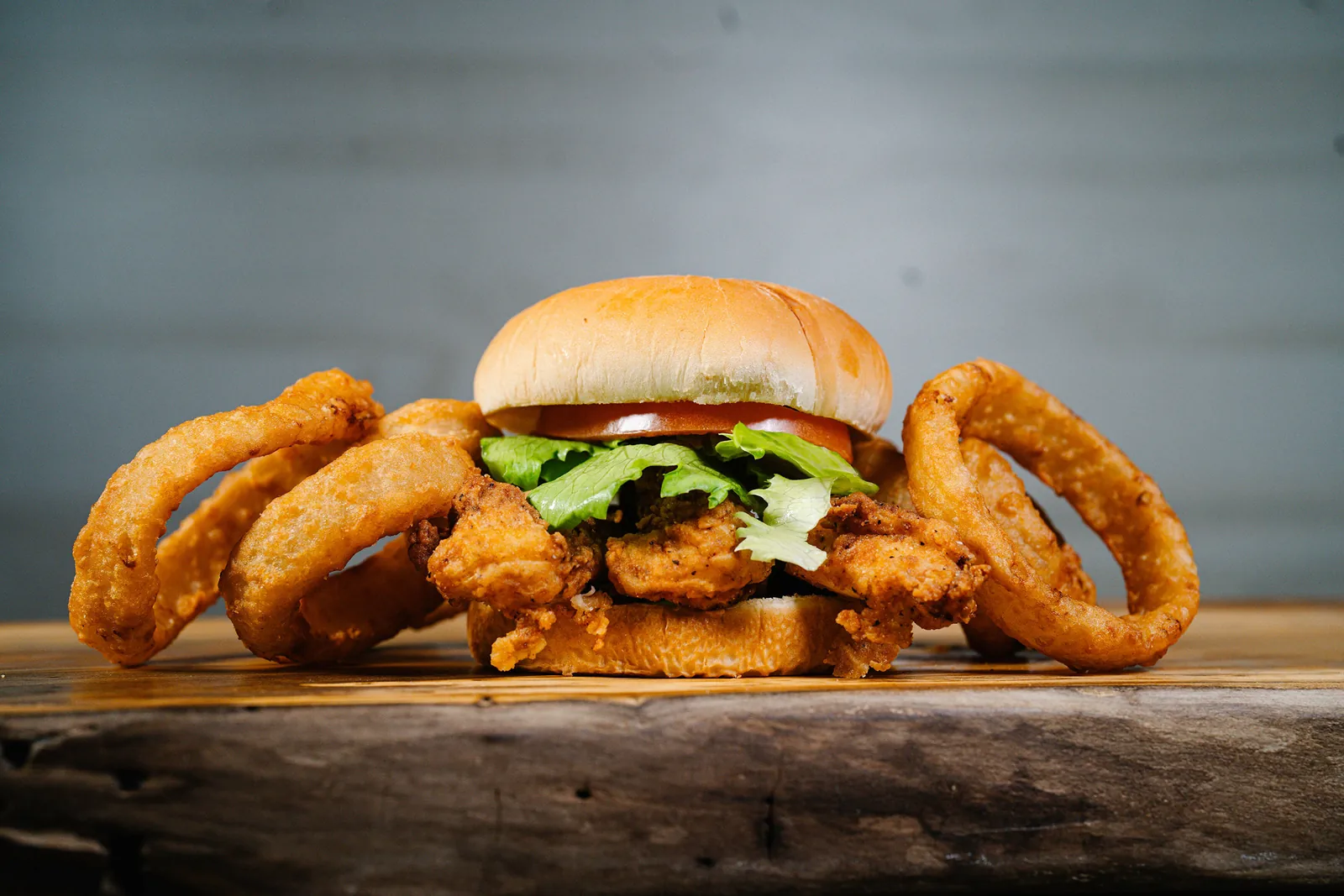 A hand-battered chicken sandwich stacked with onion rings