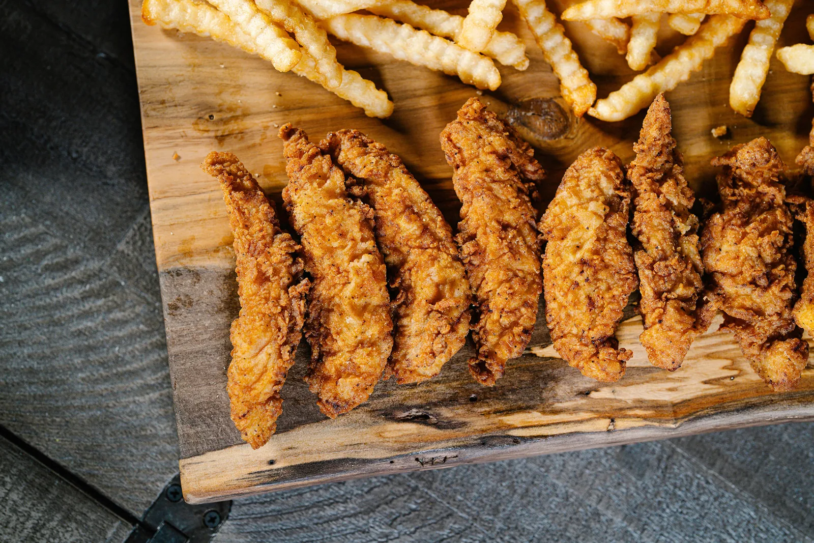 Hand-battered buttermilk chicken tenders and crinkle fries on a wooden board