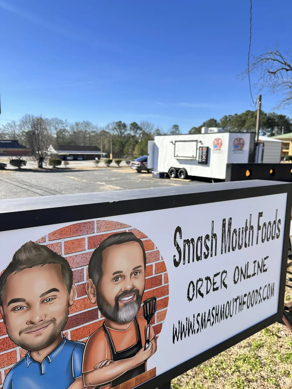 A Smash Mouth Foods roadside sign with the food trailer behind it