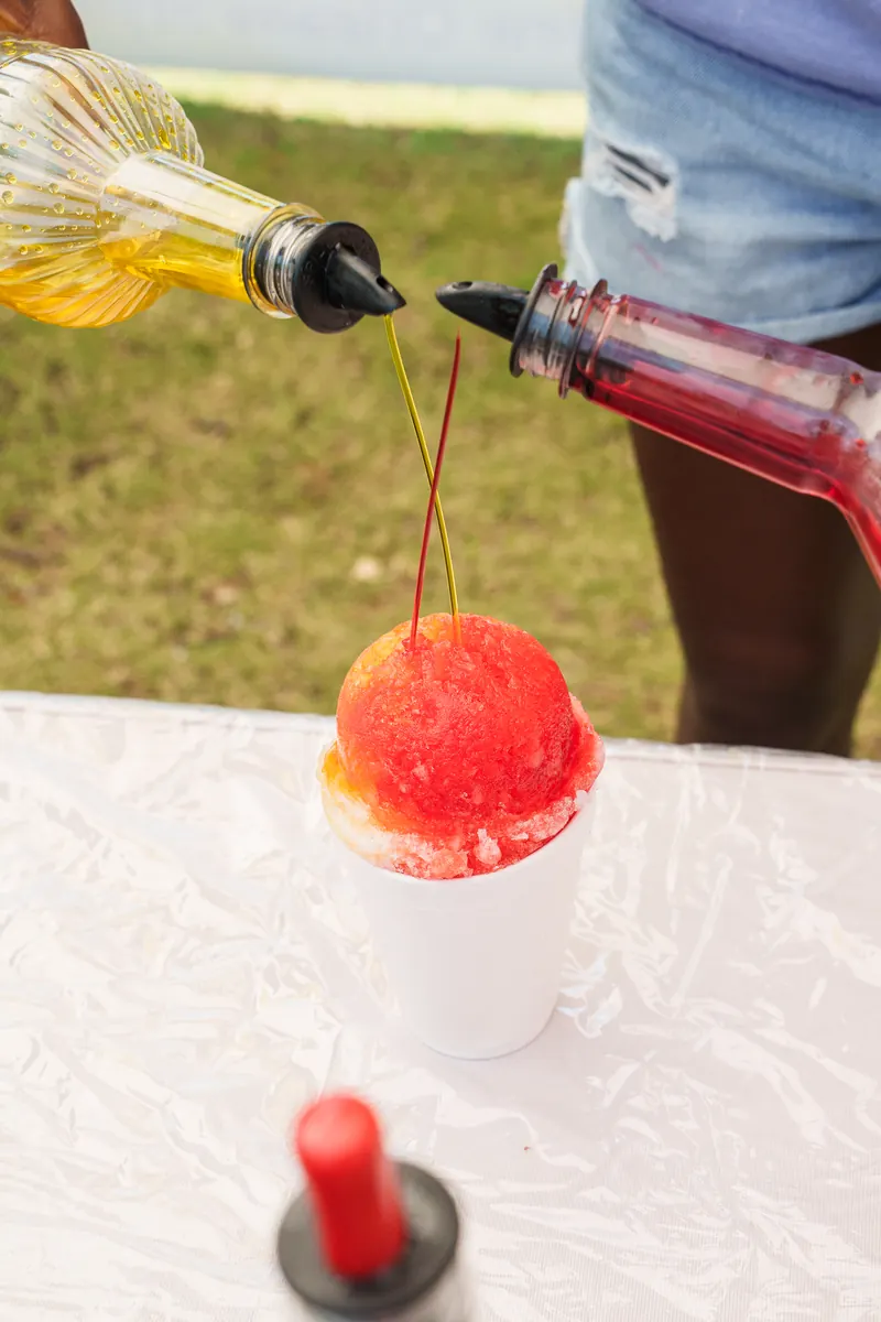 Two flavors of syrup being poured onto a red snoball at the same time