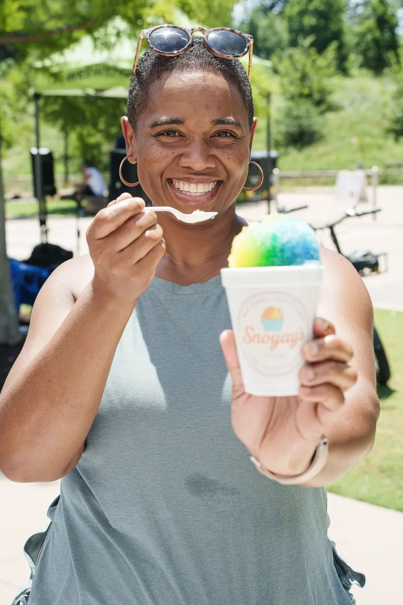 A smiling guest holding a spoonful of a blue and green snoball