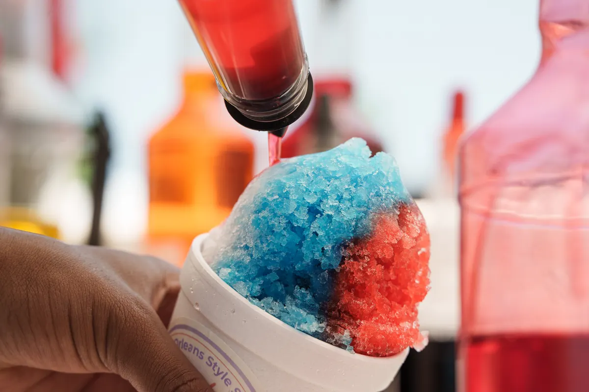 Red syrup being poured over a blue and red snoball