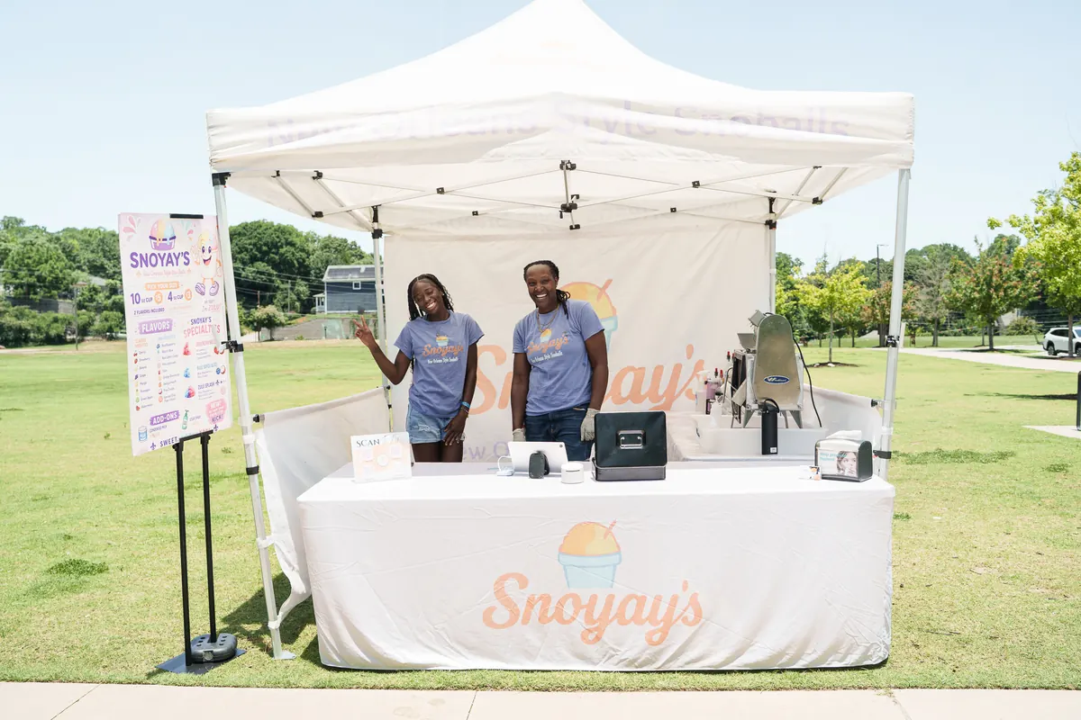 The Snoyay&rsquo;s team waving from their white event tent at an outdoor park event