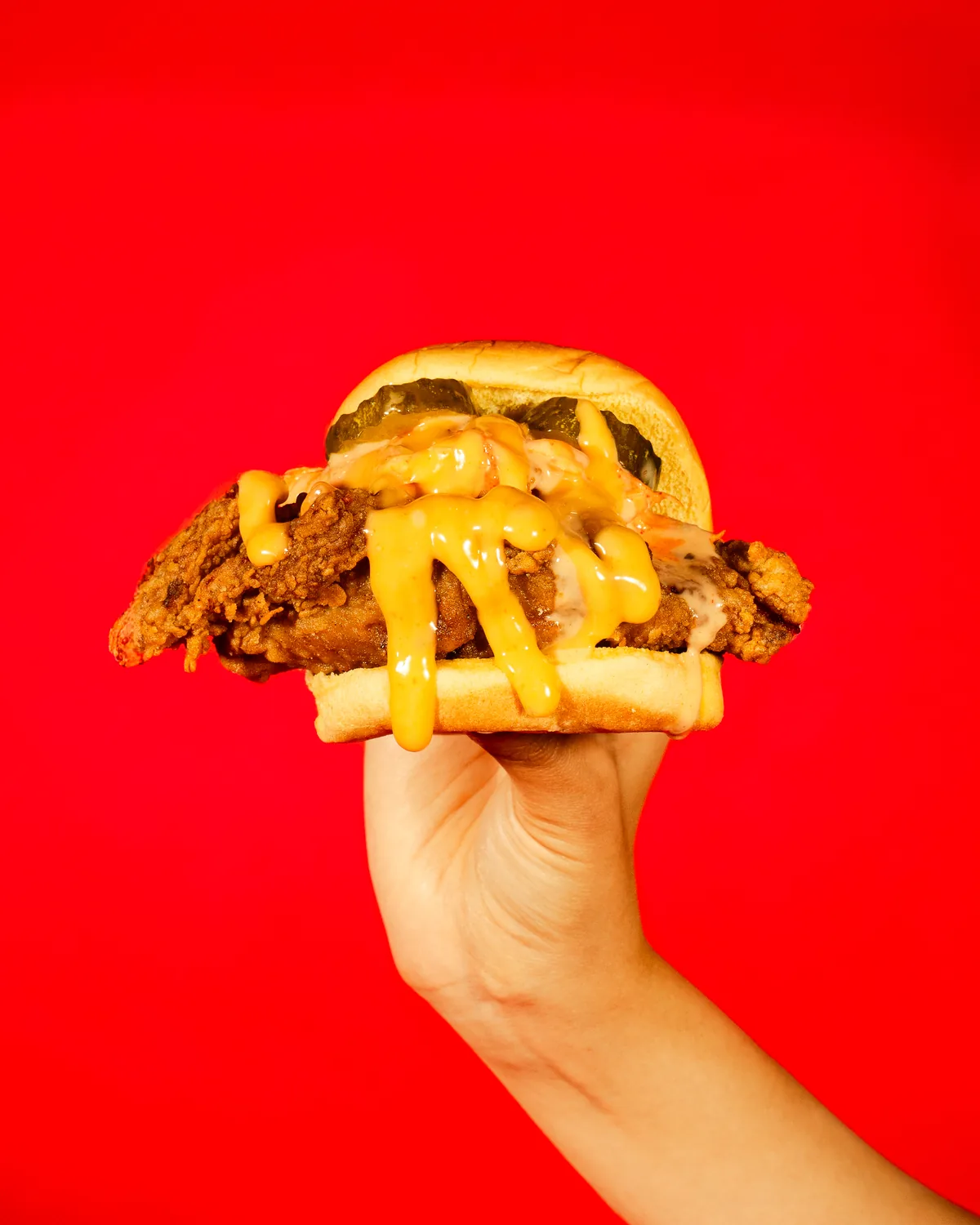 A hand holding an Ugly Chicken sandwich against a red backdrop